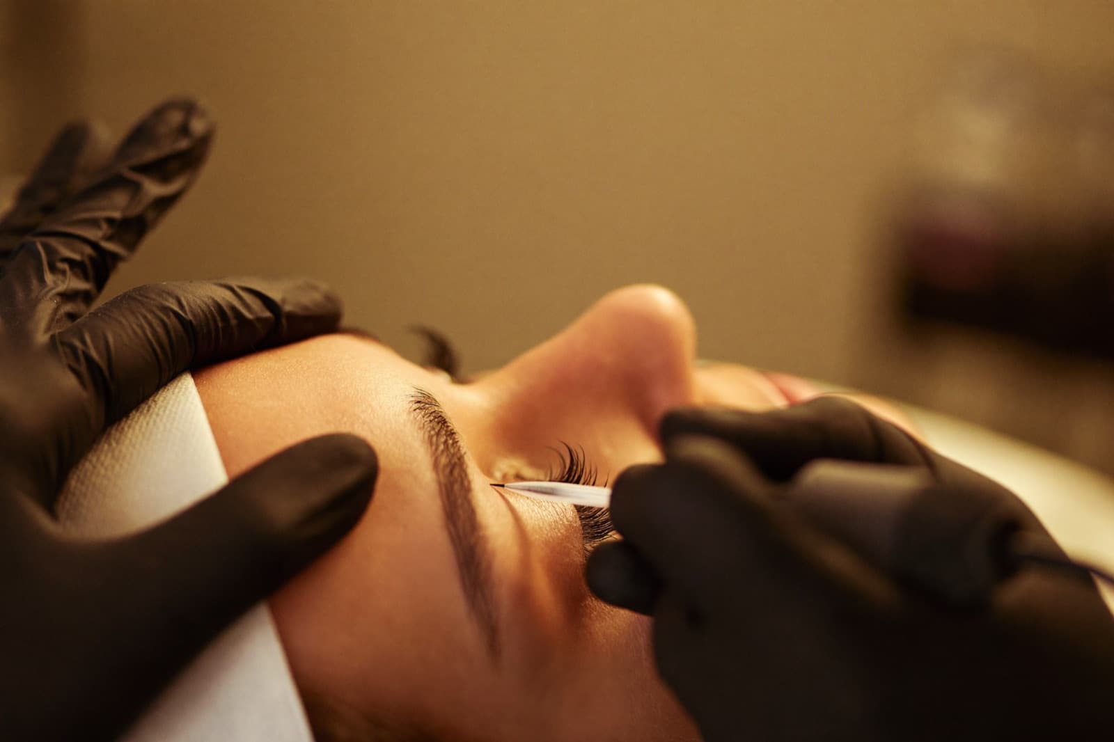 Nahaufnahme einer Microblading-Behandlung an der Augenbraue mit Handstück und schwarzen Handschuhen